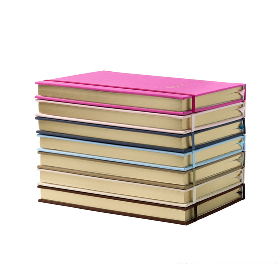 A stack of linen planners with the golden edges of the pages facing out - stacked from brown, beige, sage, blue, navy, pink to fuchsia (bottom to top). You can also see they each have a matching elastic closure
